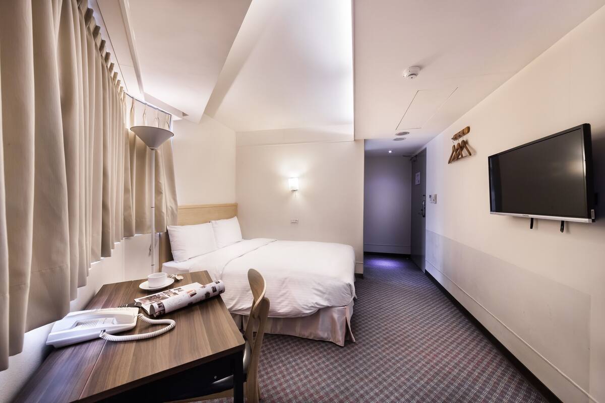 Una habitación de hotel con una cama, un escritorio, un teléfono, una taza y una revista.