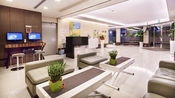 A modern hotel lobby with seating areas, a reception desk, and a large flat-screen TV.