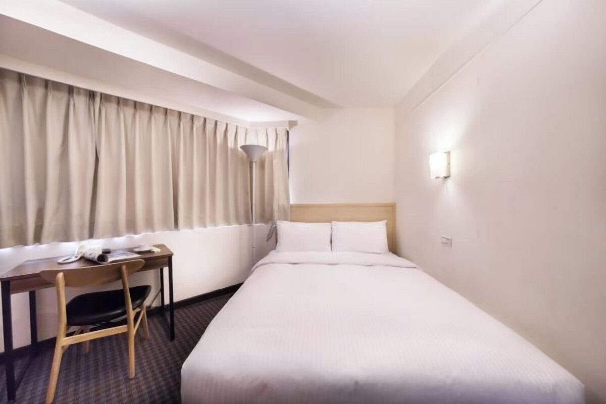A hotel room with a bed, a desk, and a chair.