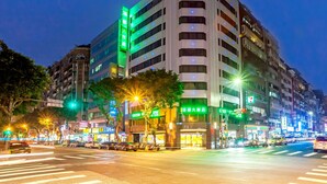 A multi-story hotel with illuminated signage, a crosswalk, and surrounding urban street.