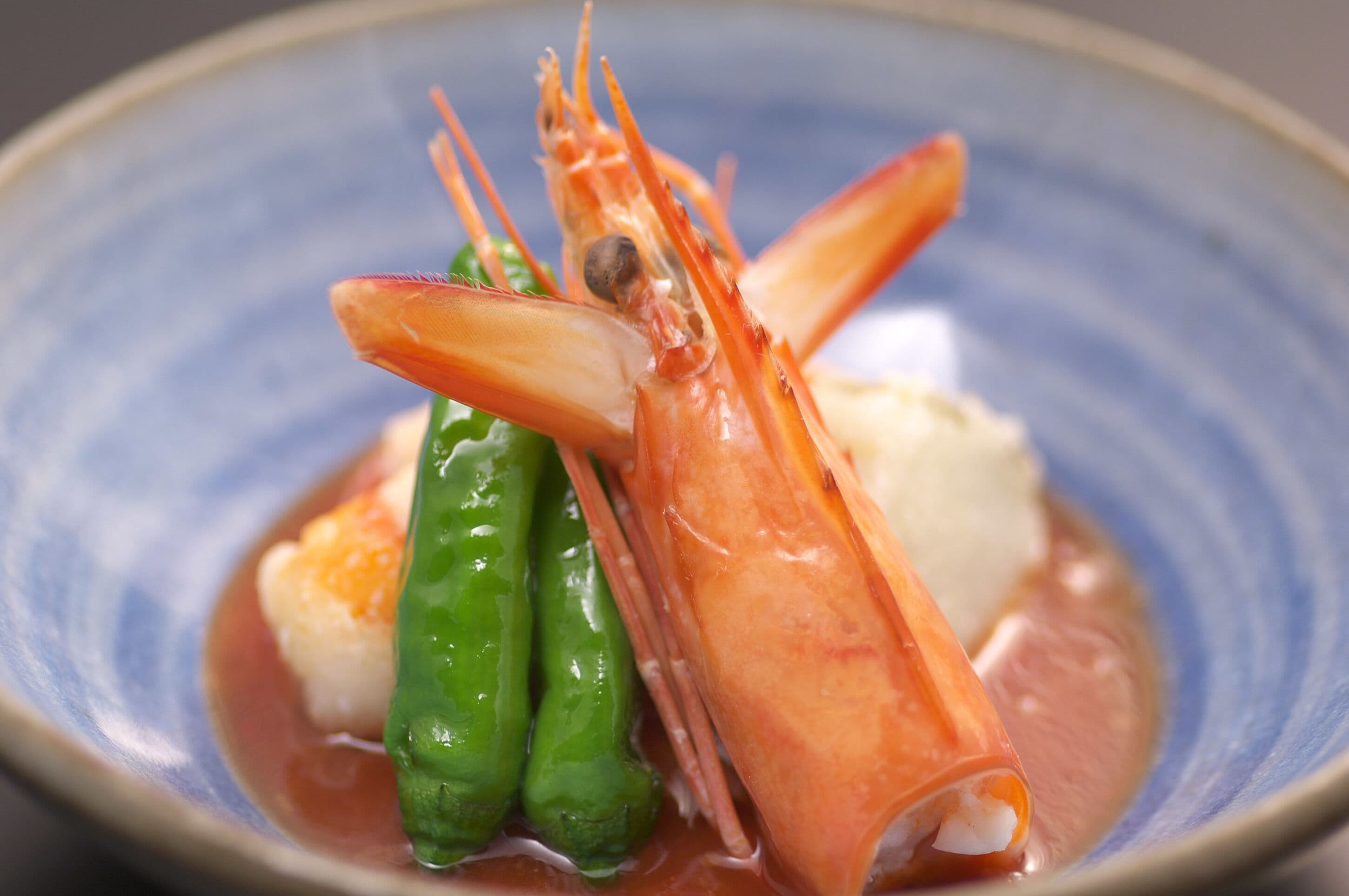 A seafood dish with shrimp, green vegetables, and a white element, served on a blue plate.
