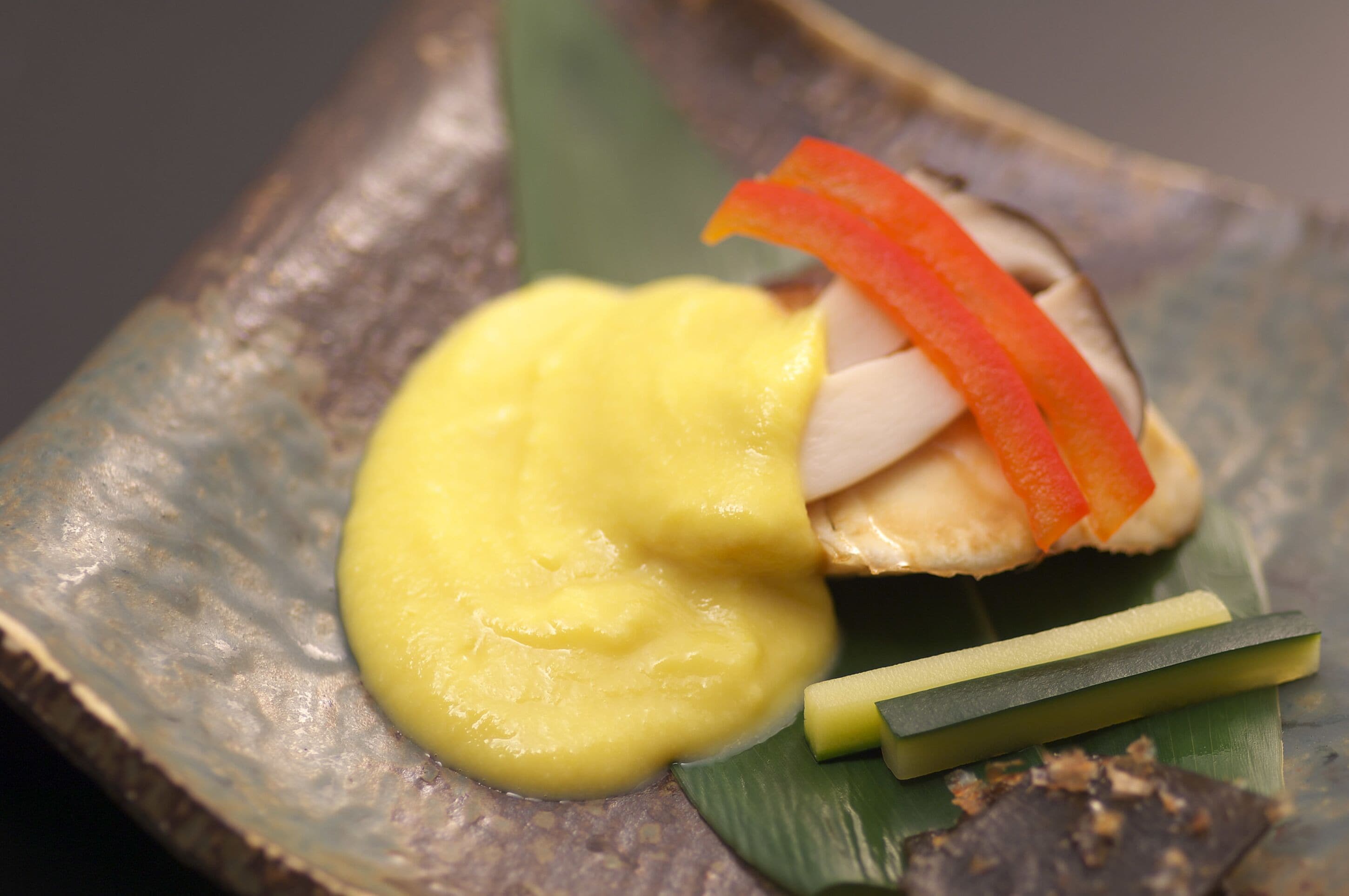 A dish with yellow sauce, red bell pepper, and green garnish on a leaf.