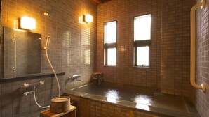 Un onsen japonés tradicional con un banco de madera, una bañera grande y una pared de azulejos.