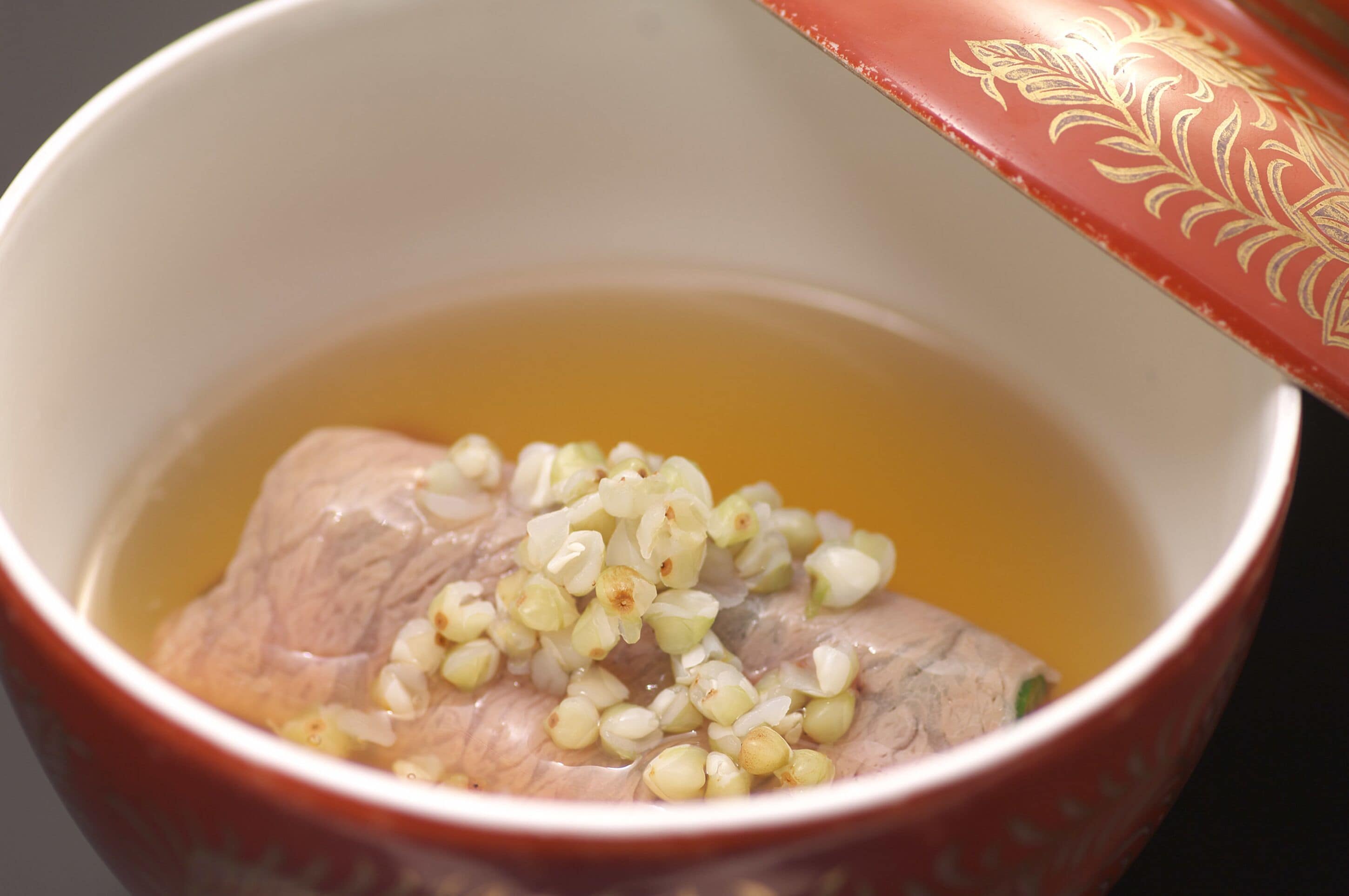 A bowl with a piece of meat and some grains in a liquid.