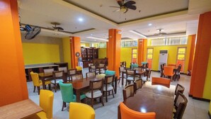 A dining area with multiple tables and chairs, ceiling fans, and a bright yellow and orange color scheme. - One Averee Bay Hotel (Coron)