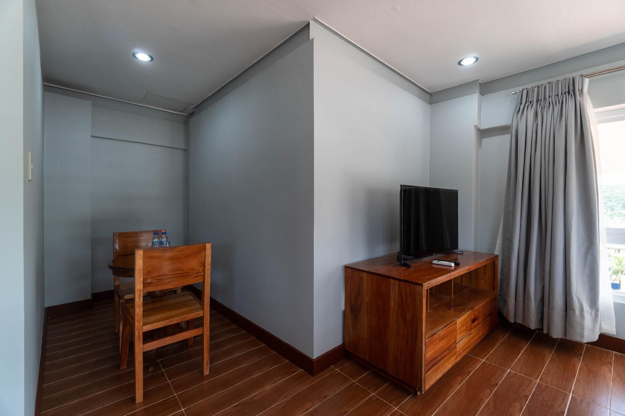 A room with a wooden desk, a chair, a television, and a window with curtains.