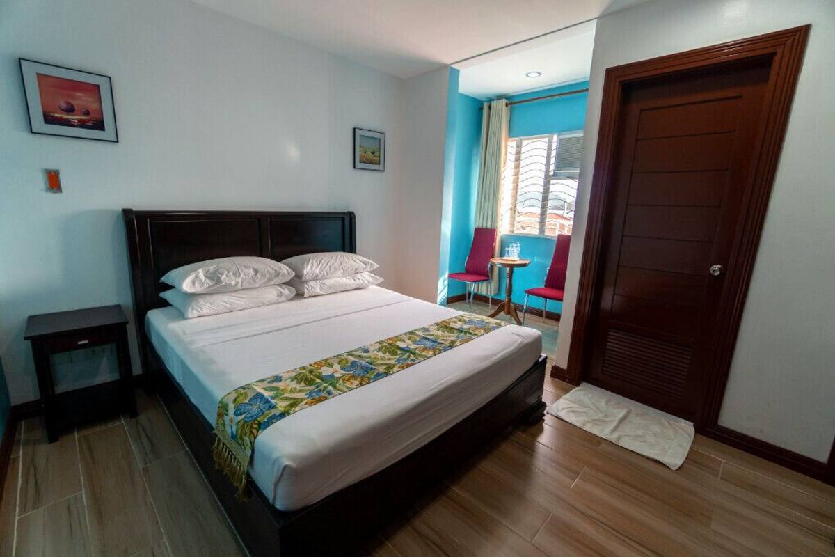 A bedroom with a large bed, a nightstand, a chair, a small table, and a door.
