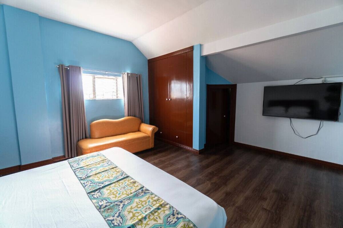 A hotel room with a bed, a sofa, a wardrobe, and a TV.