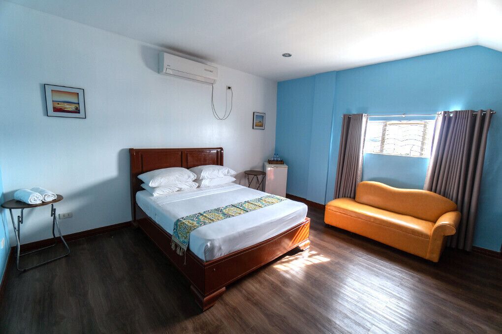 A bedroom with a wooden bed, a sofa, a small table, and a window with curtains.