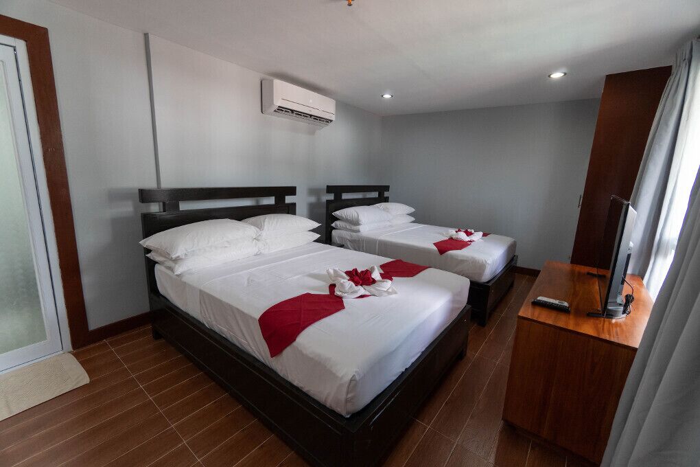 A hotel room with two beds, a TV, and an air conditioning unit.