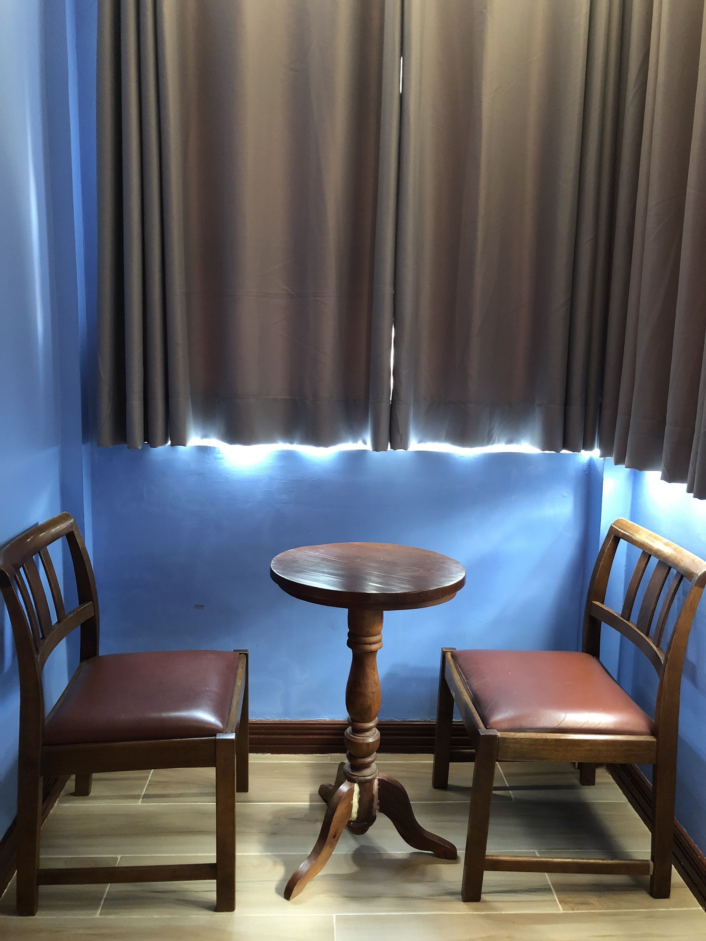 A corner room with a wooden table and two chairs, blue walls, and a window with curtains.