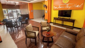 A hotel lobby with wicker furniture, a brown leather sofa, a TV, and a fan. - One Averee Bay Hotel (Coron)