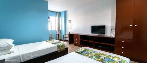 Habitación de hotel con dos camas, televisión, armario y ventana con cortinas.