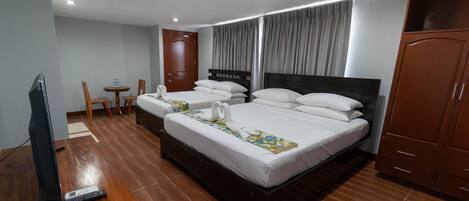 Una habitación de hotel con una cama grande, un televisor, una mesita con sillas y un armario.