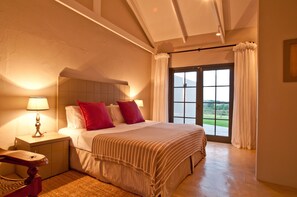 A bedroom with a large bed, a nightstand, a lamp, and a view of the outdoors through a window. - Kay and Monty Vineyard View (The Crags)