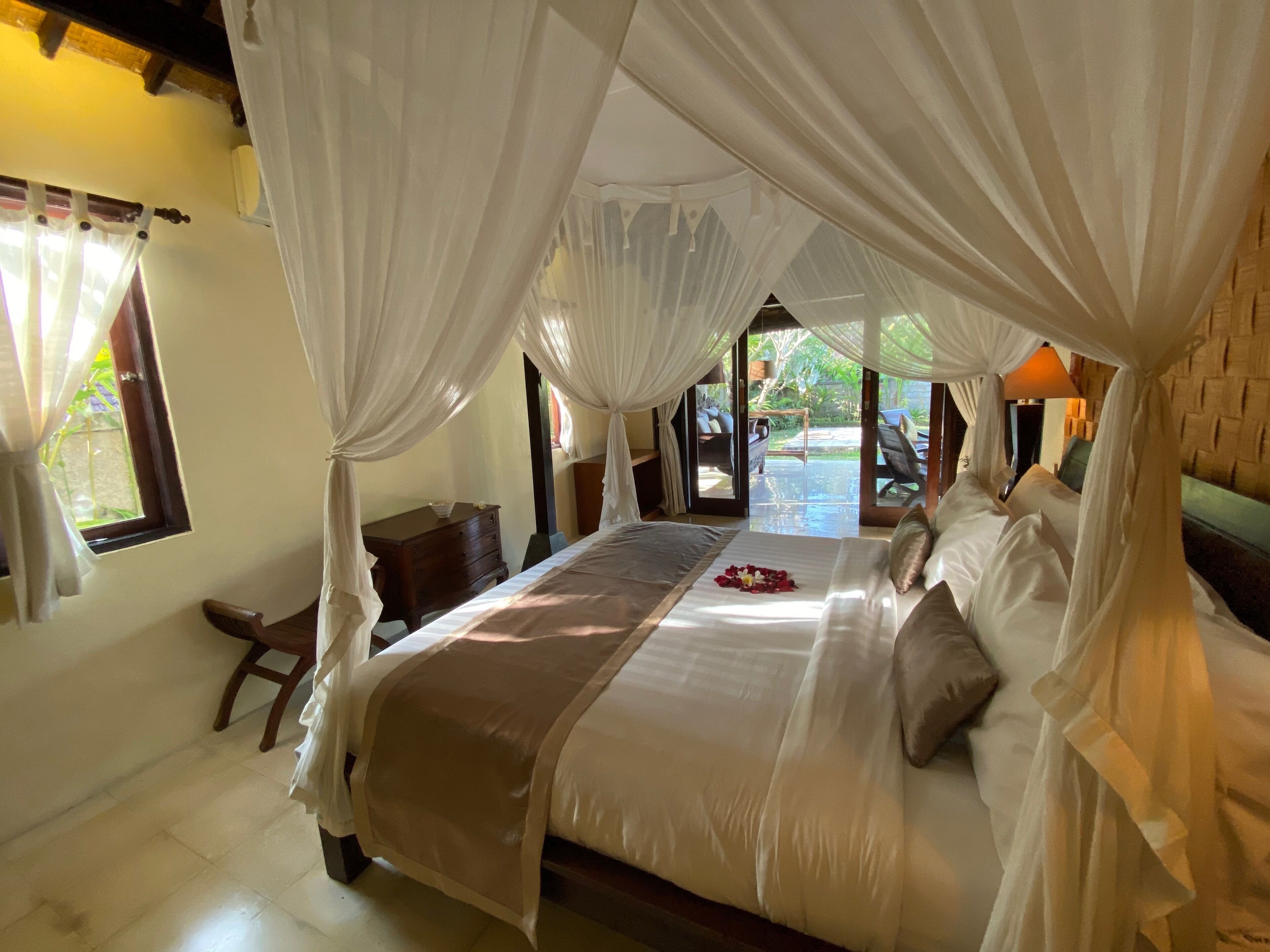 A bedroom with a large bed, white curtains, and a view of the outdoors.