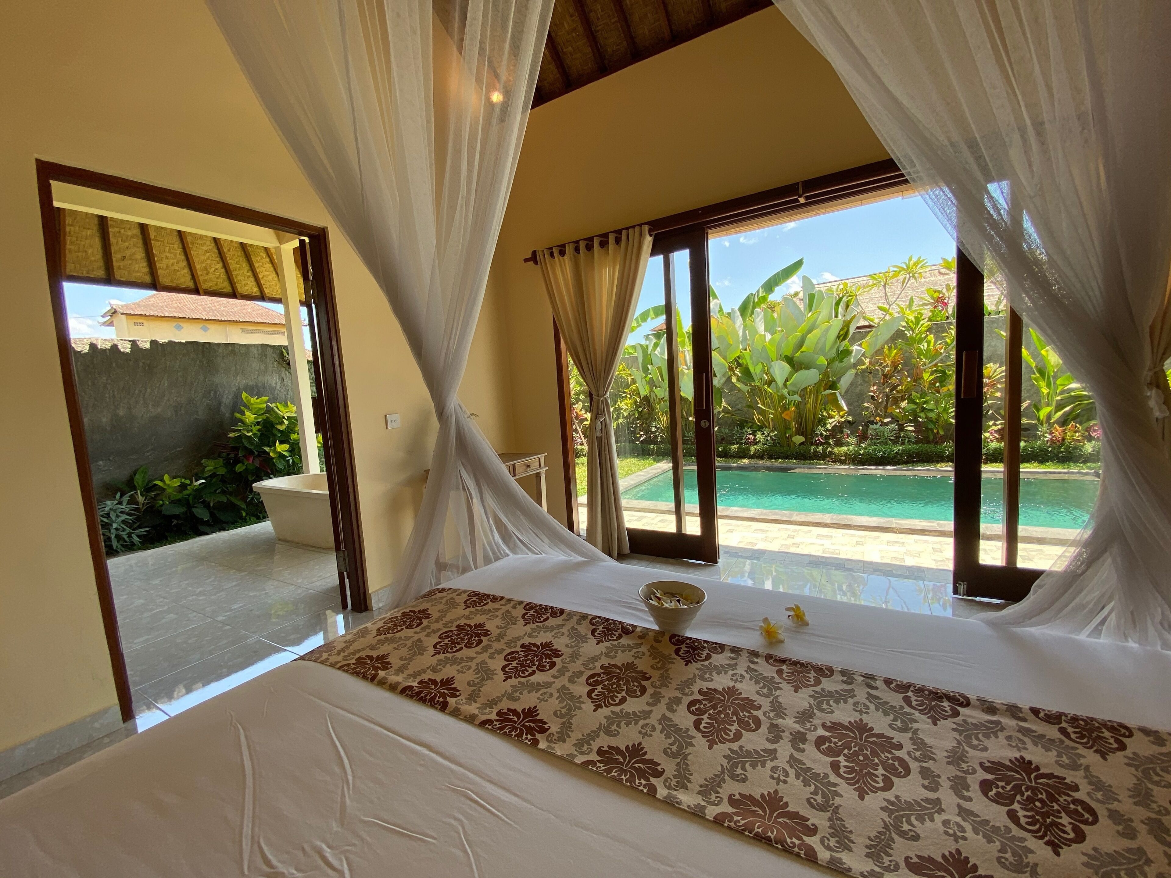 A bedroom with a bed, a view of a swimming pool, and a balcony.