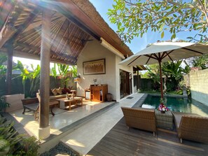 A covered outdoor seating area with a pool, wooden furniture, and tropical plants. - Rumah Dadong (Ubud)