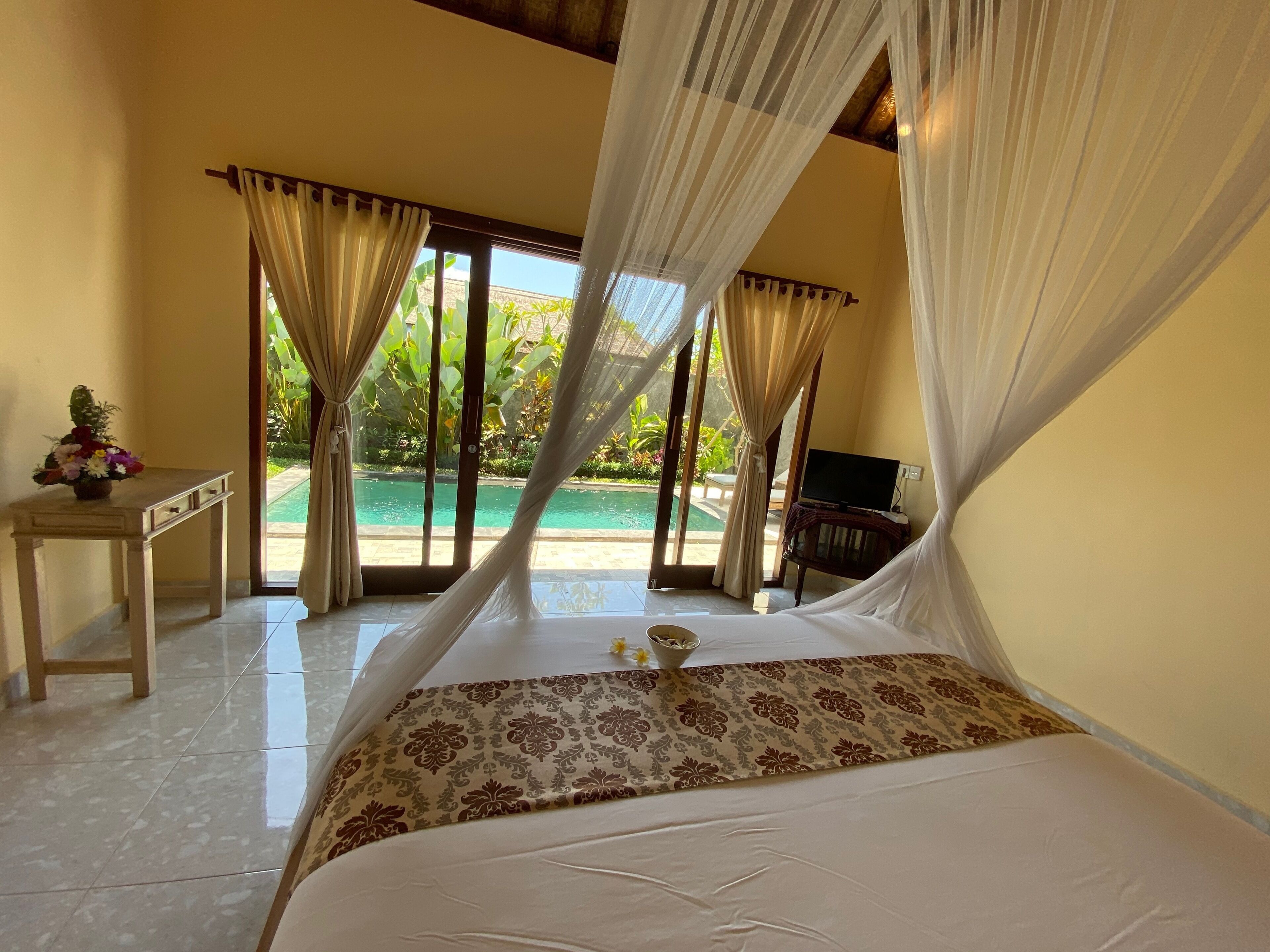 Ein Schlafzimmer mit Bett, Schreibtisch, Fernseher und Blick auf einen Swimmingpool.