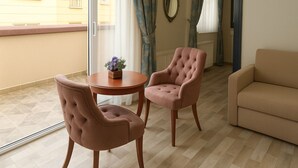 Ein Zimmer mit einer Couch, zwei Sesseln, einem kleinen runden Tisch mit einer Vase und einem Fenster mit Vorhängen.