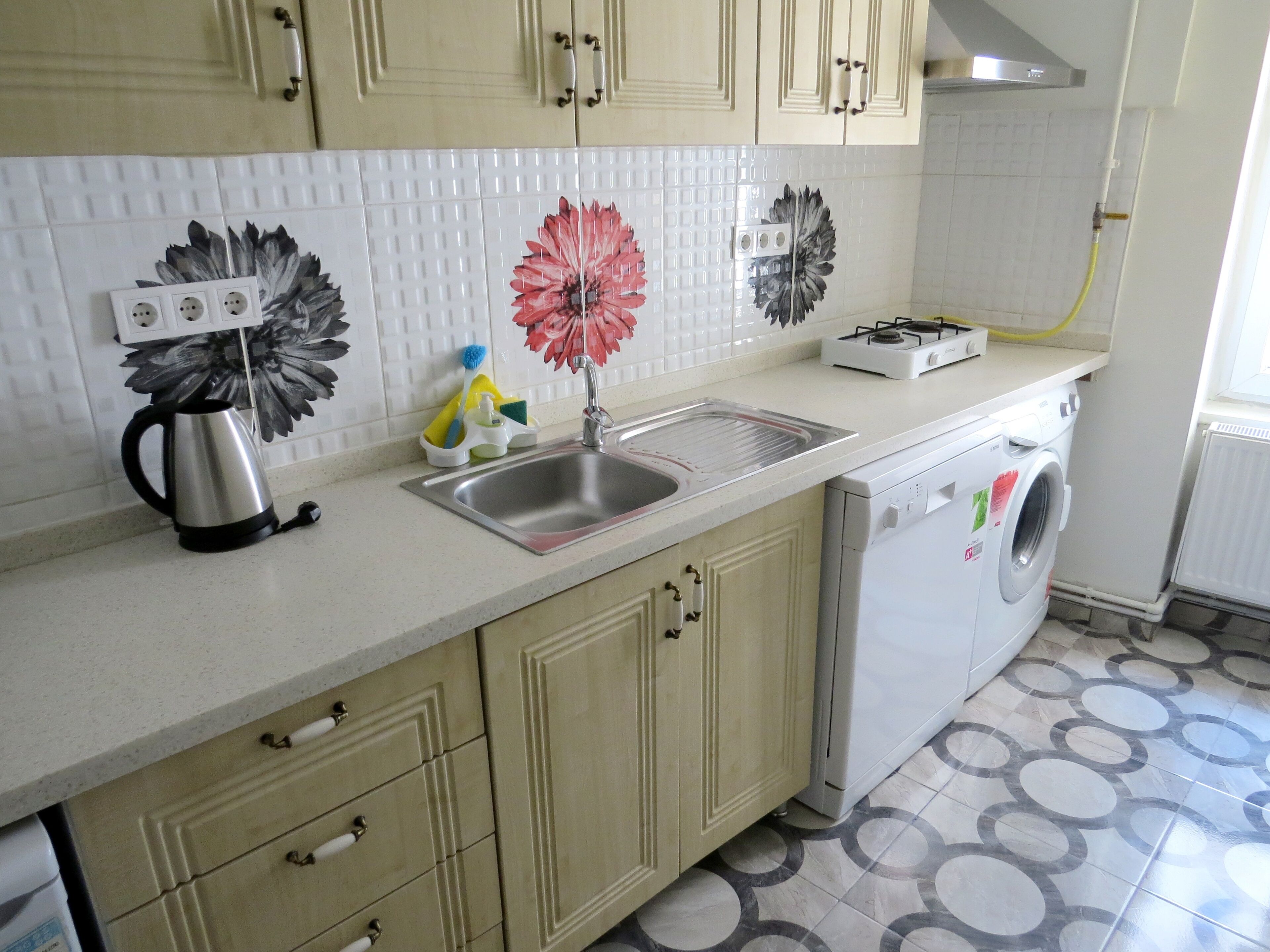 A kitchen with a sink, a kettle, a washing machine, and a gas stove.
