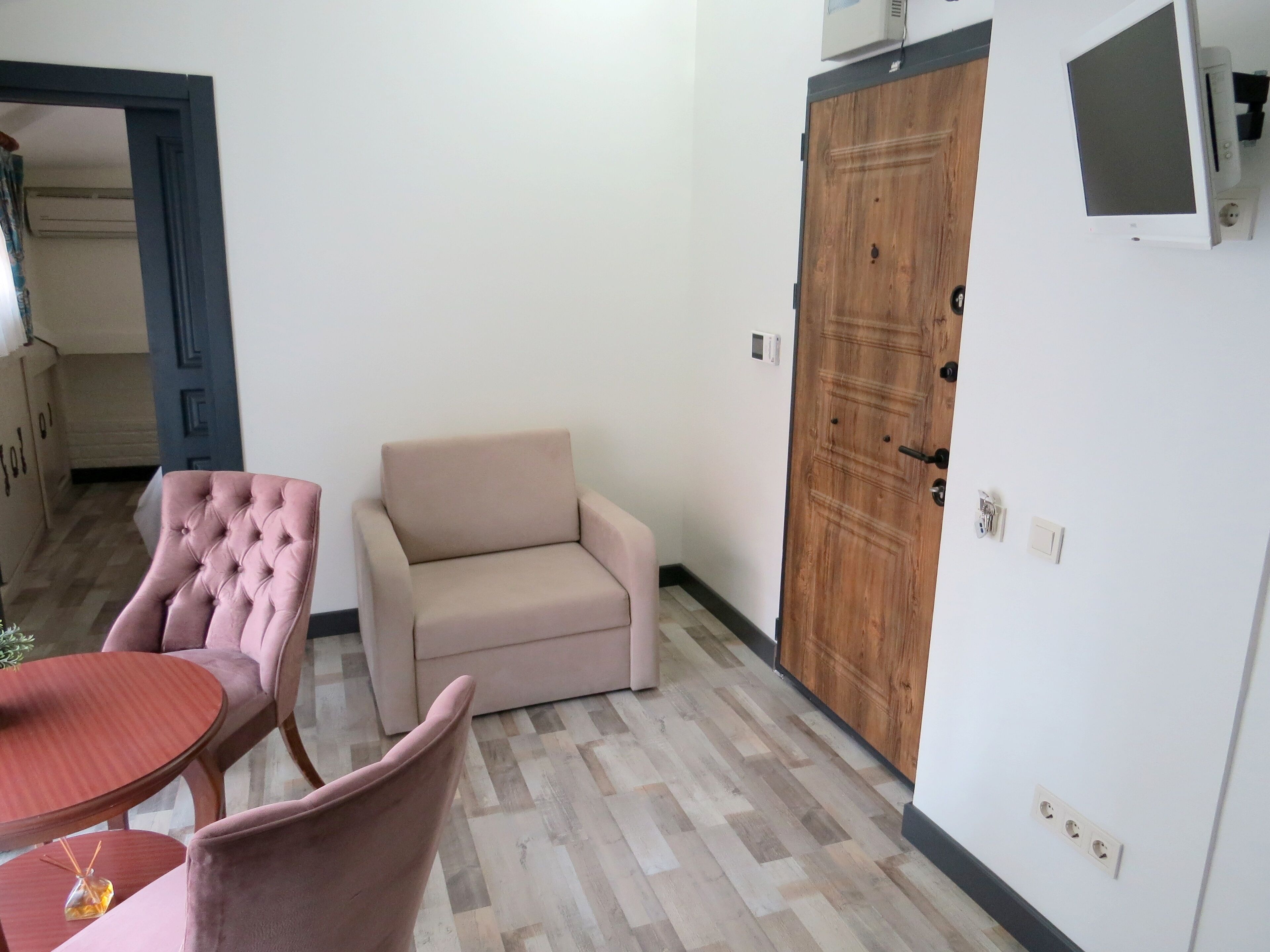 A room with a wooden floor, a beige sofa, a pink armchair, and a small round table.