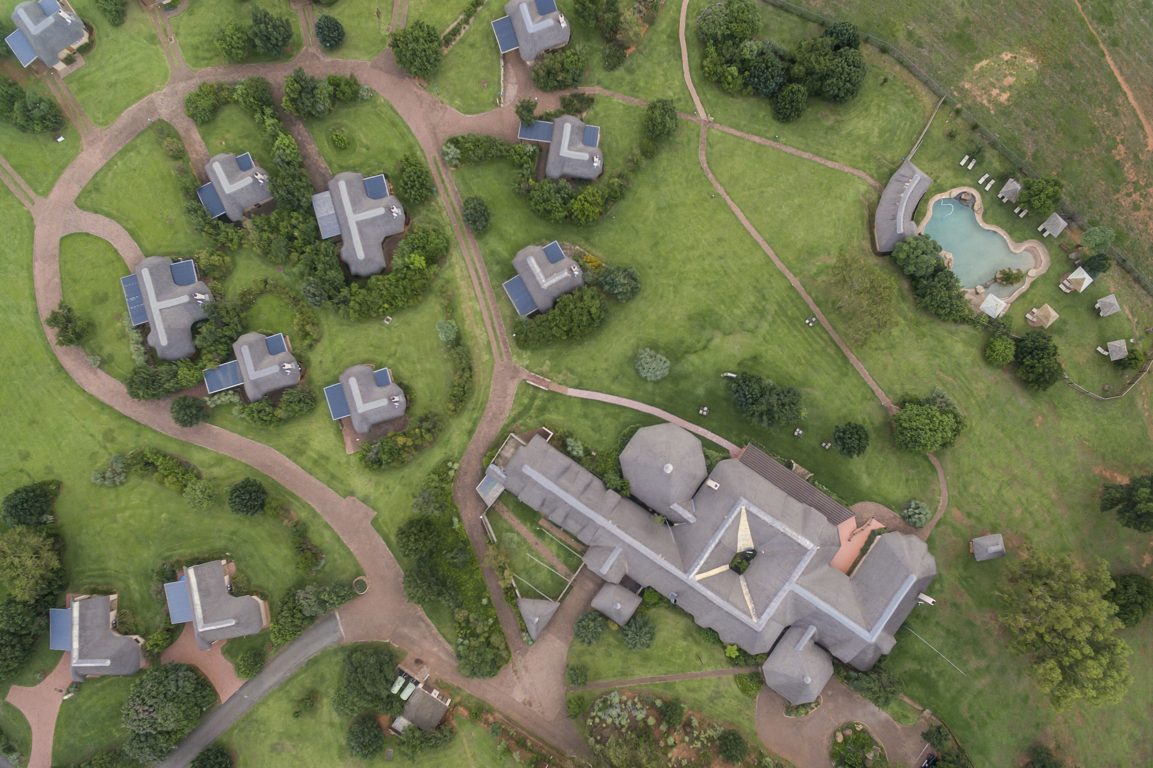 Vista aérea de una zona residencial con varias casas, un edificio grande con un tejado distintivo y una piscina.