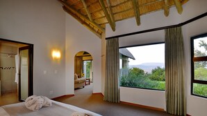 A hotel room with a large bed, a mirror, a window with curtains, and a view of the outdoors. - Montusi Mountain Lodge (Jagersrust)