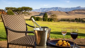 A wicker chair with a metal bucket and two glasses of wine on a table, with a scenic view of mountains in the background. - Montusi Mountain Lodge (Jagersrust)
