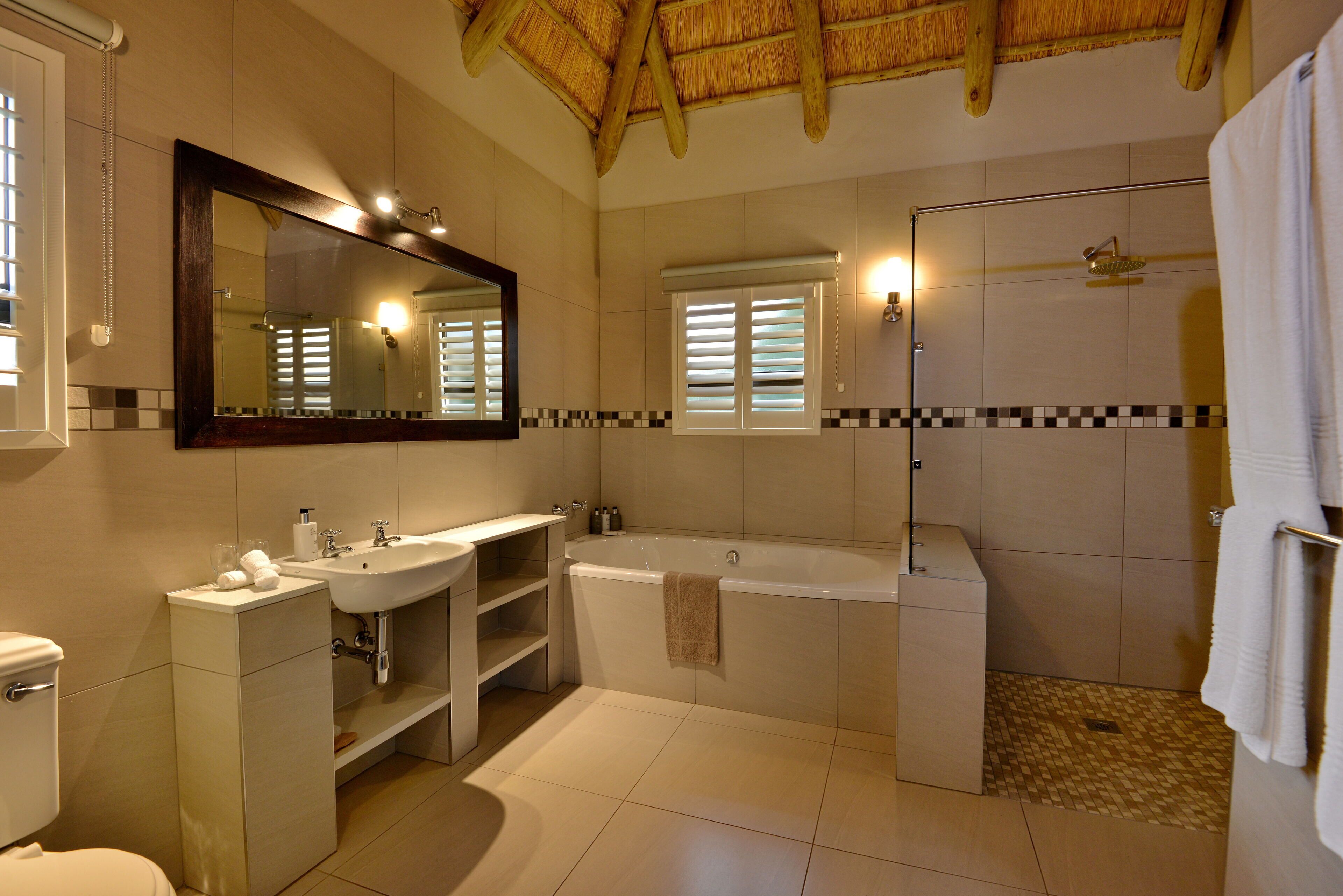 A modern bathroom with a large mirror, a bathtub, a shower, and a toilet.
