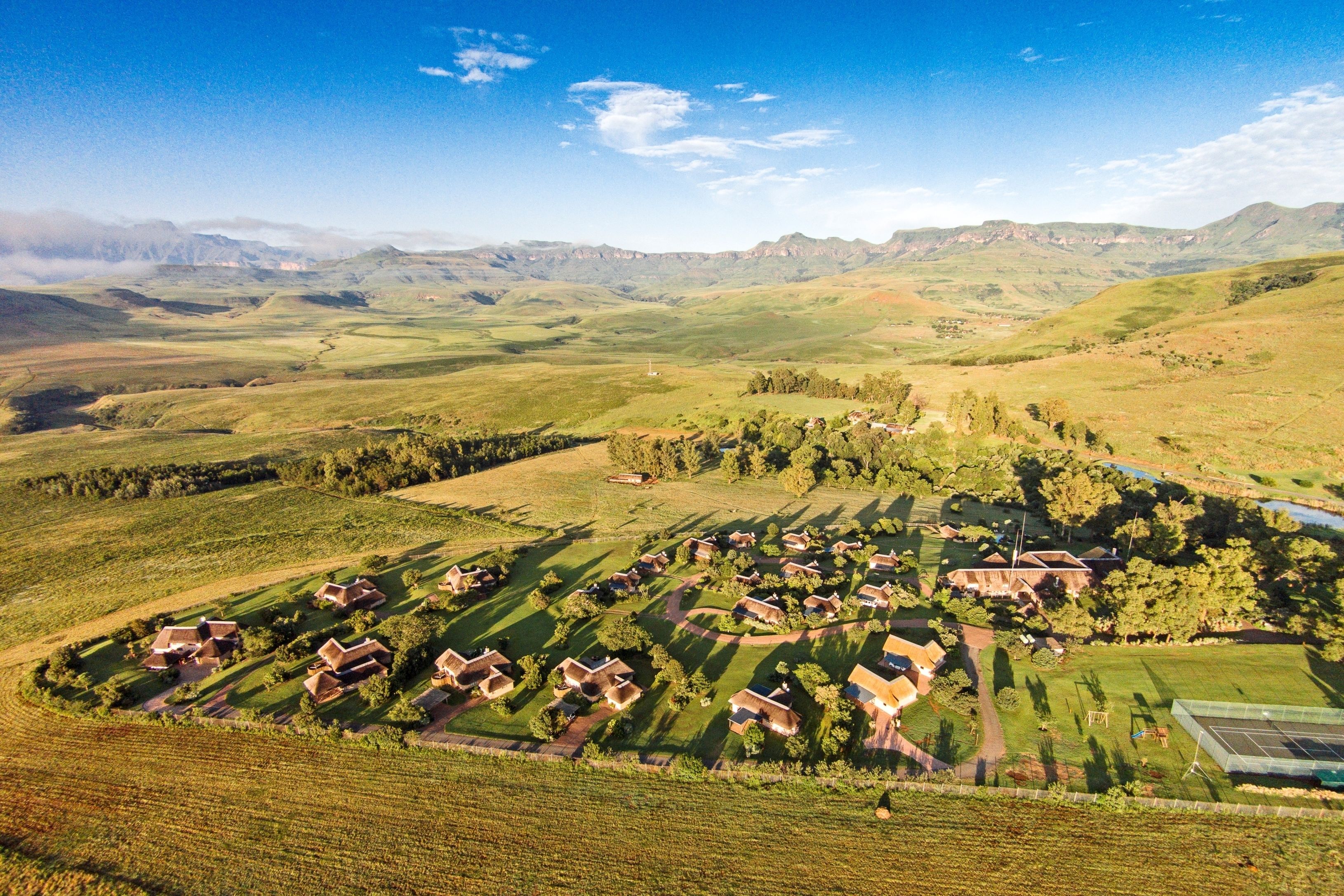 Un paisaje rural con un conjunto de casas rodeado de campos y montañas al fondo.