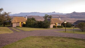 A rural landscape with thatched-roof cottages, a paved driveway, and a view of distant mountains. - Montusi Mountain Lodge (Jagersrust)