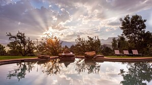 A serene outdoor pool area with a clear reflection of trees and the sky, surrounded by lounge chairs and a stone pathway. - Montusi Mountain Lodge (Jagersrust)