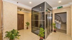 Un lobby moderno con un ascensor de vidrio, una puerta de madera y plantas en macetas.
