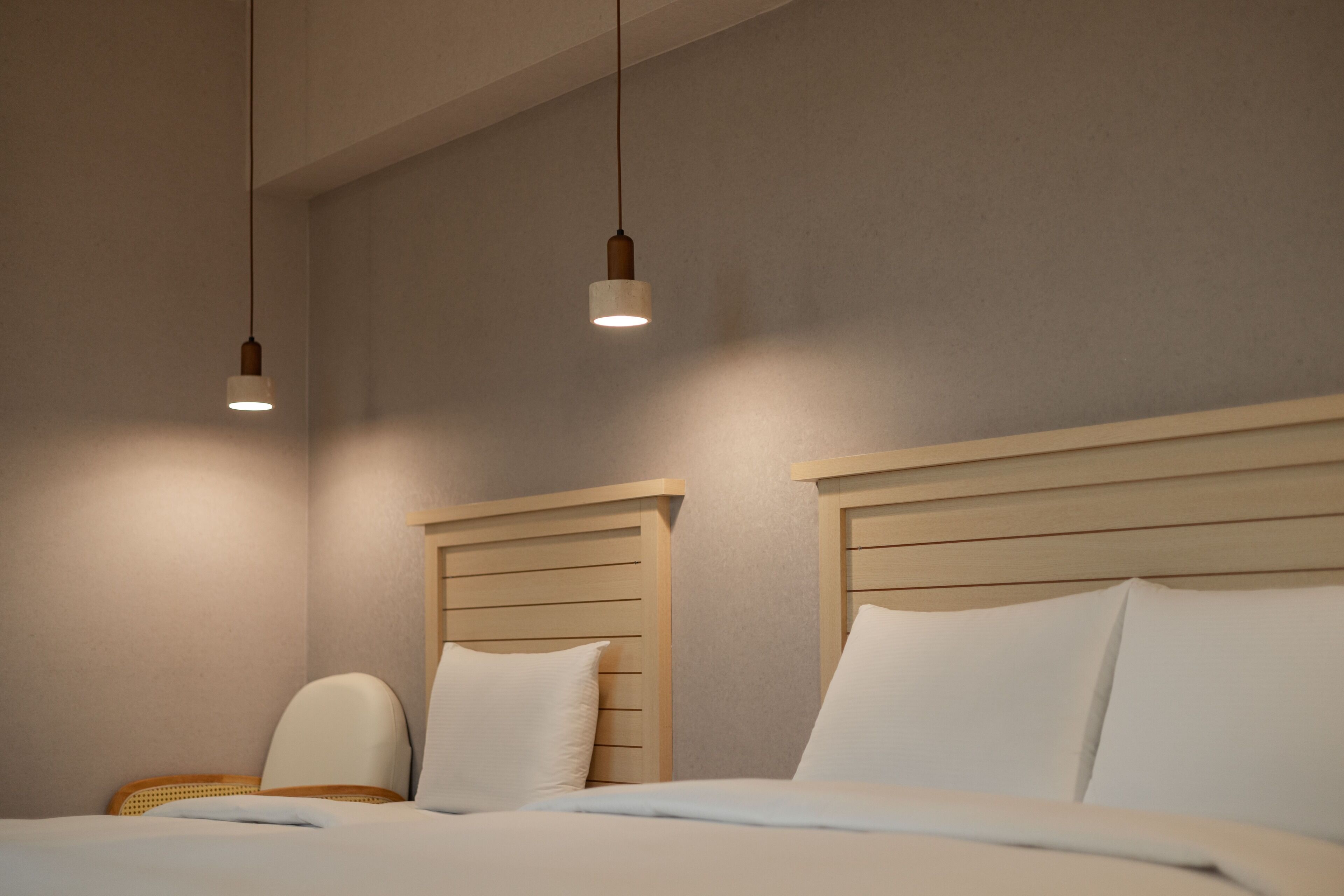 A hotel room with a wooden headboard, a single bed with white bedding, and two pendant lights.