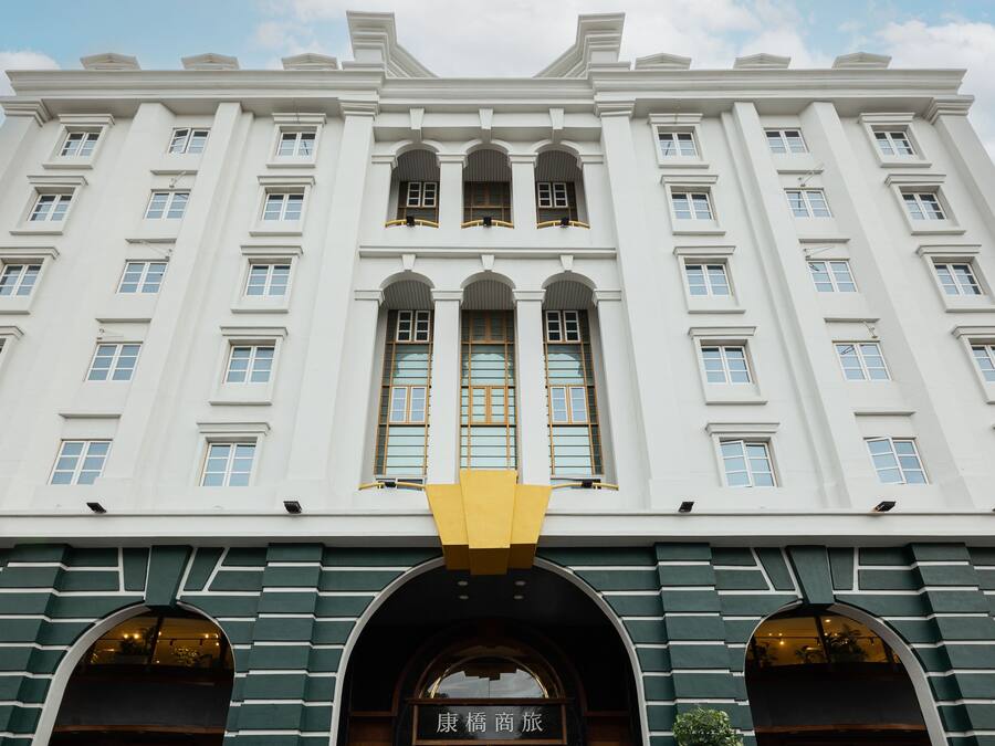 Um edifício grande e branco, com várias janelas e uma entrada central com uma placa.
