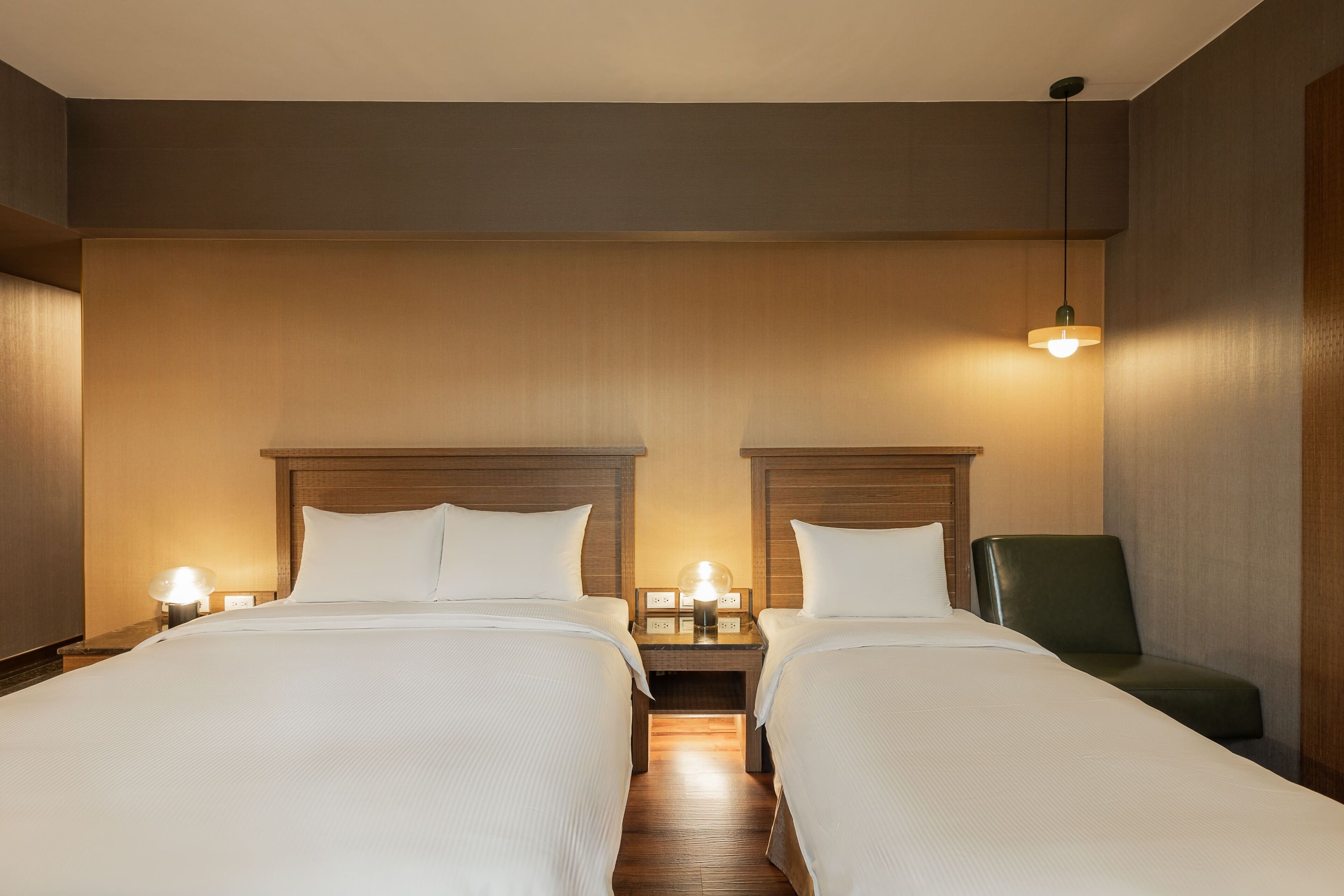 Una habitación de hotel con dos camas, mesitas de noche, una lámpara y una silla.