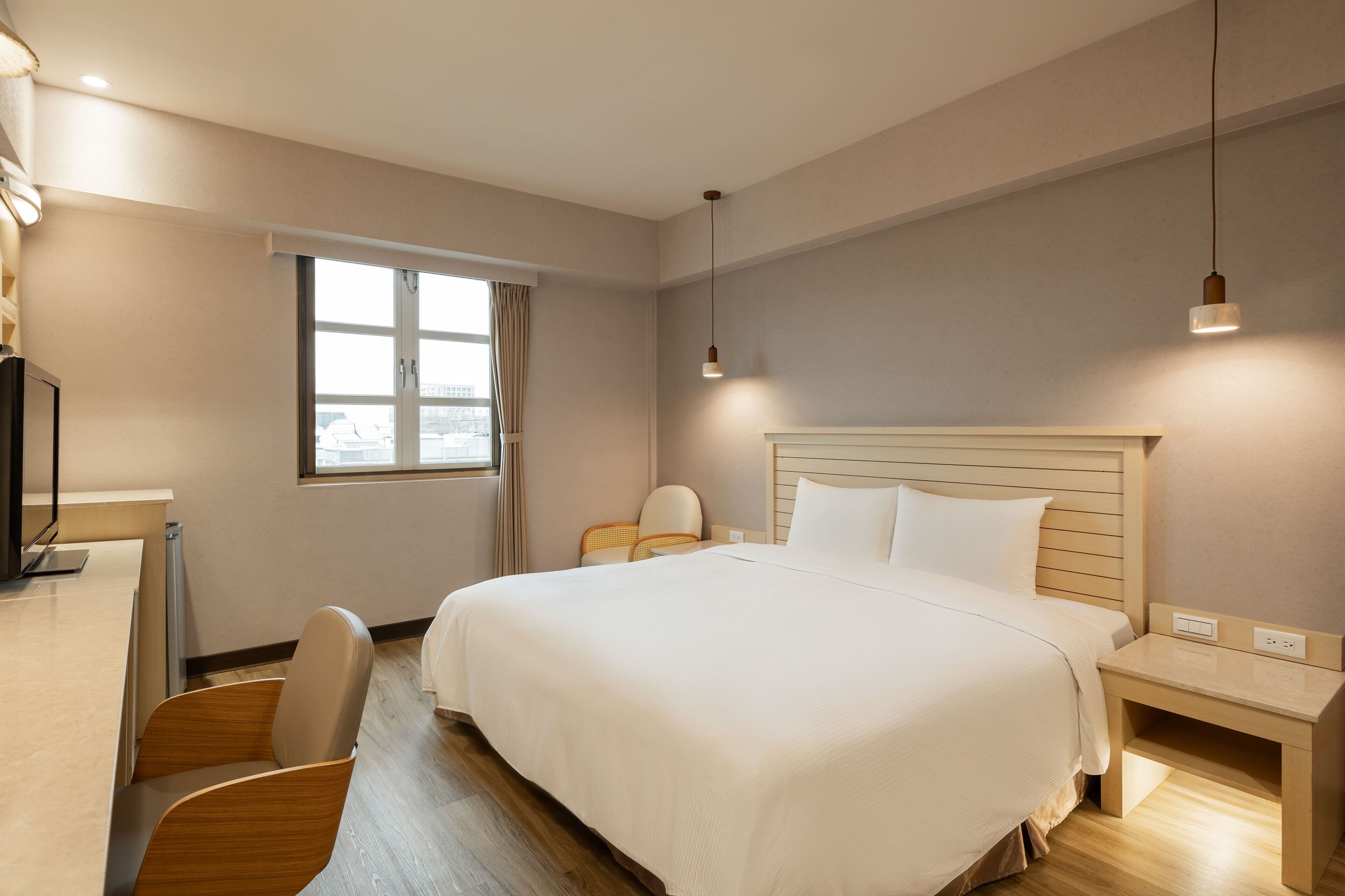 A modern hotel room with a large bed, a desk, and a chair.