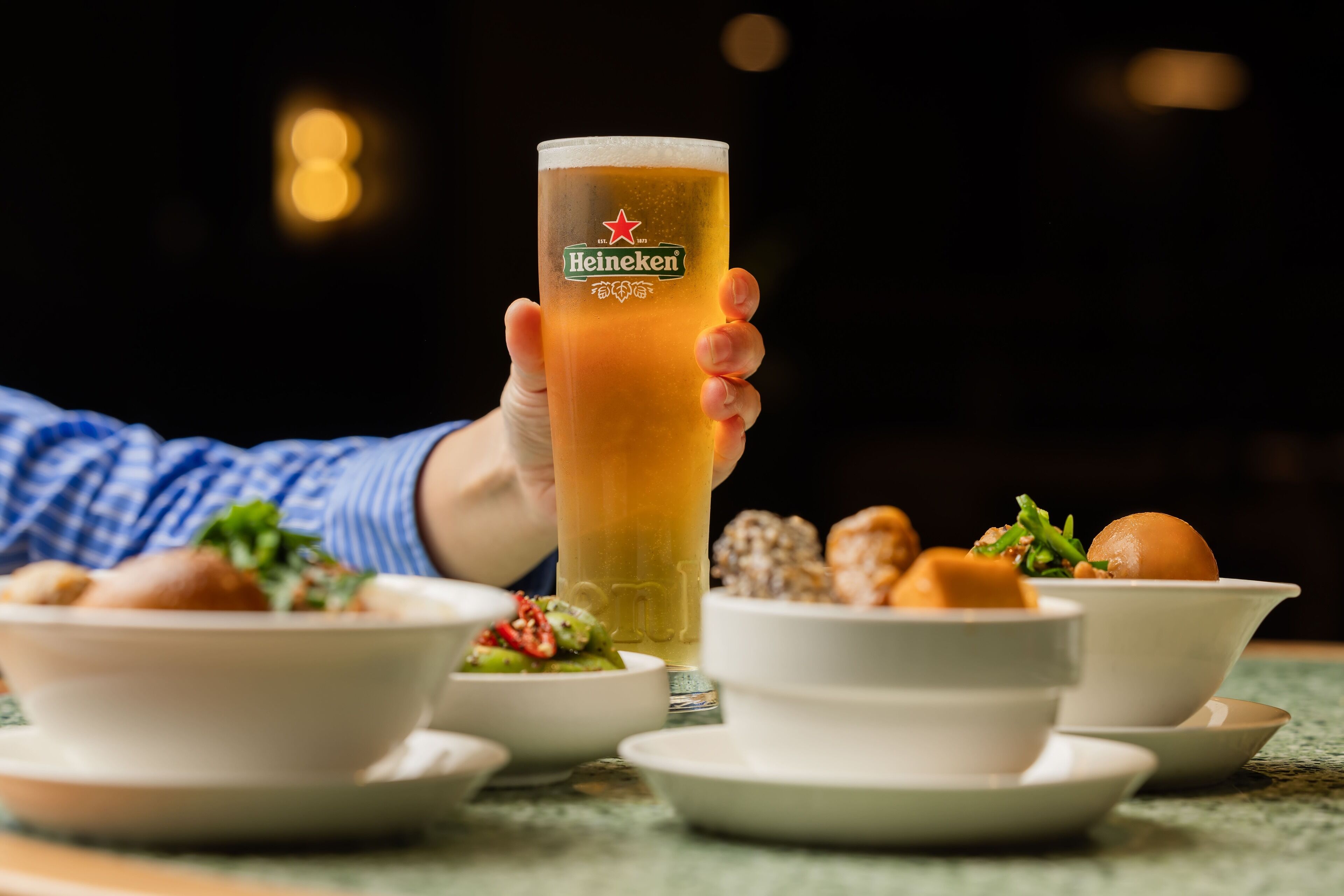 A person holding a Heineken glass with a dark background.