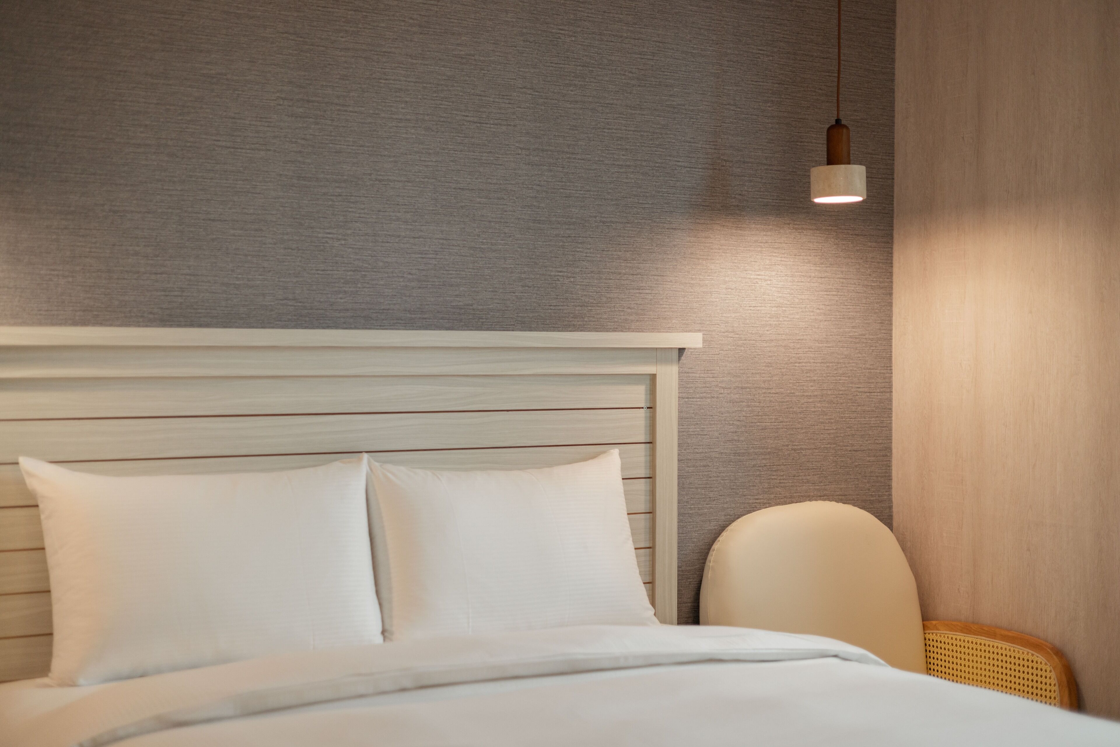 Una cama bien tendida con sábanas y almohadas blancas, un cabecero de madera y una lámpara de noche.