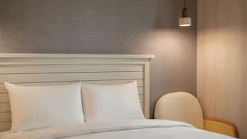 Una cama bien tendida con sábanas y almohadas blancas, un cabecero de madera y una lámpara de noche.