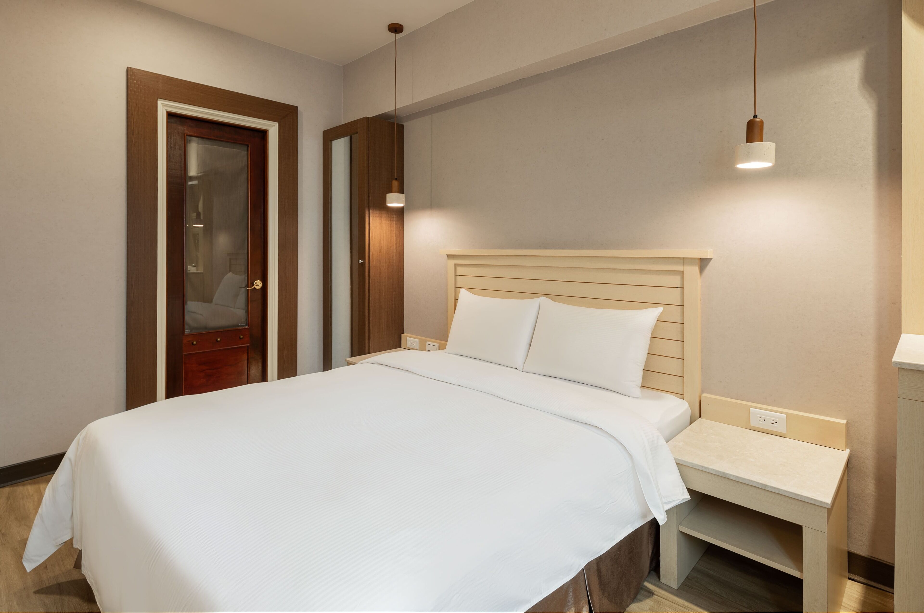 A neatly made bed with a wooden headboard, a bedside table with a lamp, and a door with a mirror.