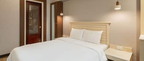 A neatly made bed with a wooden headboard, a bedside table with a lamp, and a door with a mirror.