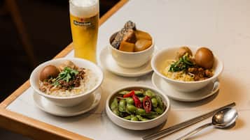 Una bandeja con cuatro platos de comida, una cerveza en un vaso y una cuchara sobre una mesa.
