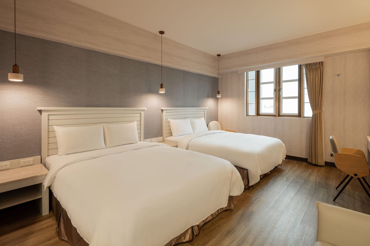 Quarto de hotel com duas camas, uma mesa e uma cadeira.