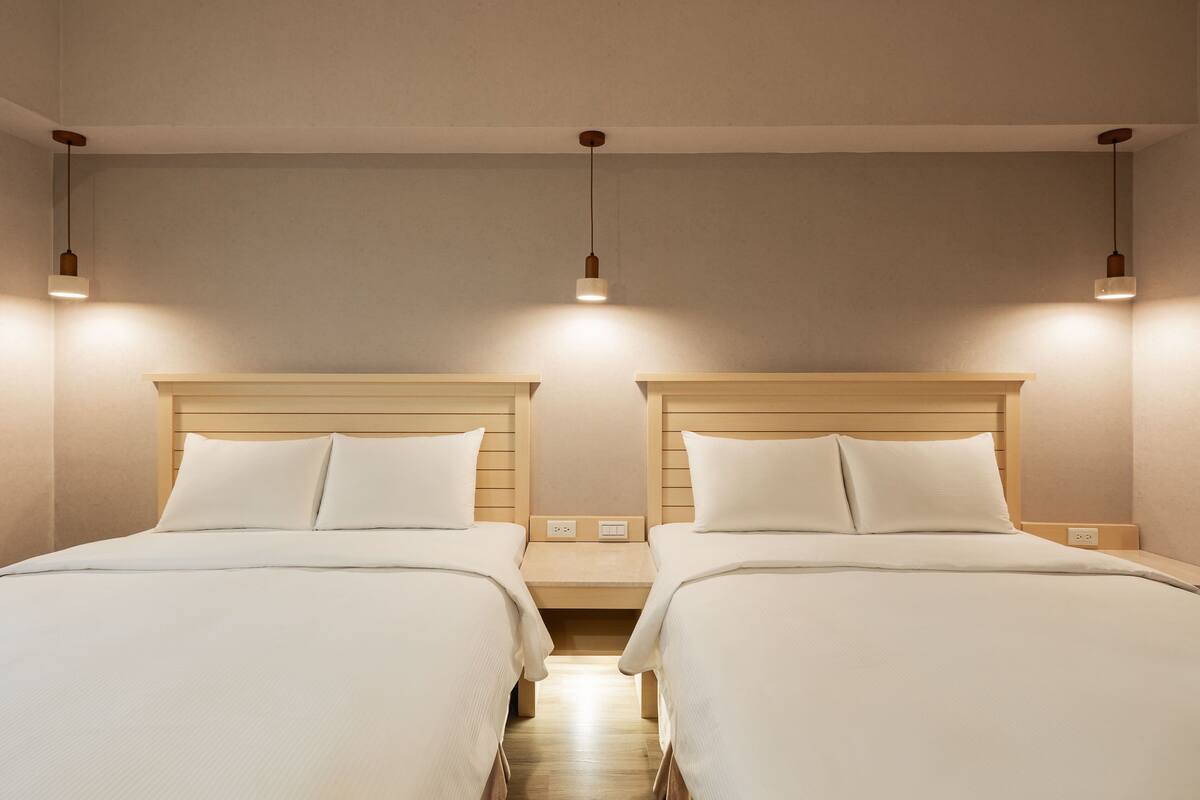 Quarto de hotel com duas camas, cabeceiras de madeira e iluminação pendente.