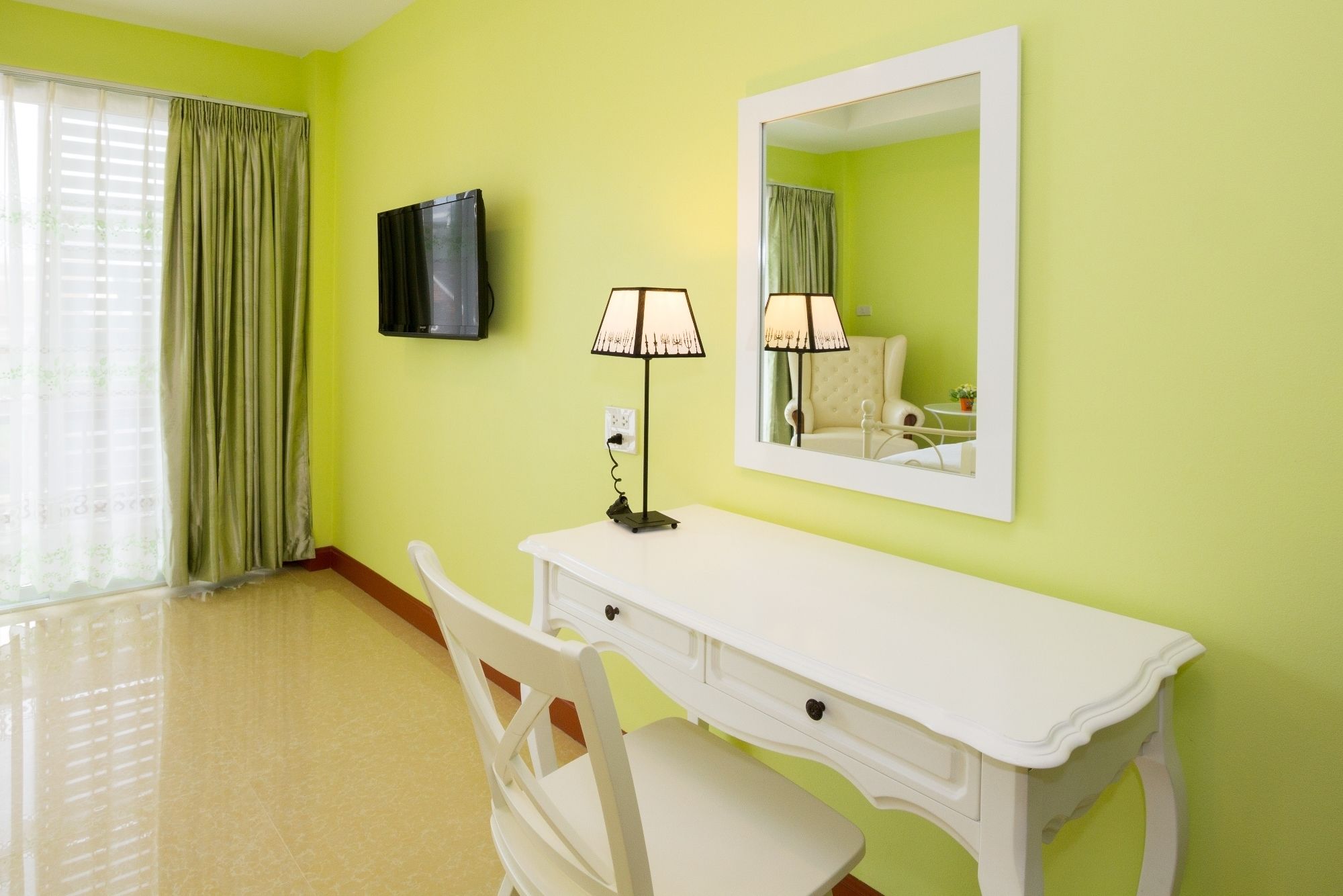 A room with a white desk, a mirror, a television, and a lamp.