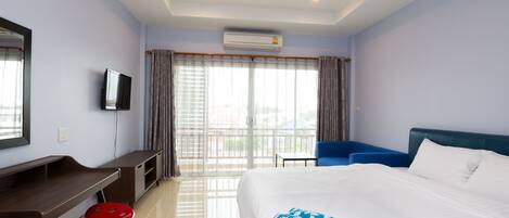 A hotel room with a bed, a desk, a chair, a television, and a balcony with curtains.
