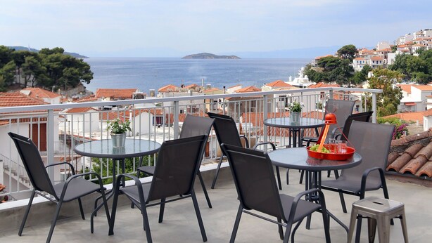 Una terraza con una mesa redonda y sillas, con vistas a un pueblo costero con edificios y el mar.