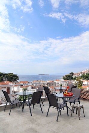 Une terrasse avec une table ronde et des chaises, donnant sur une ville côtière avec ses bâtiments et offrant une vue sur la mer.